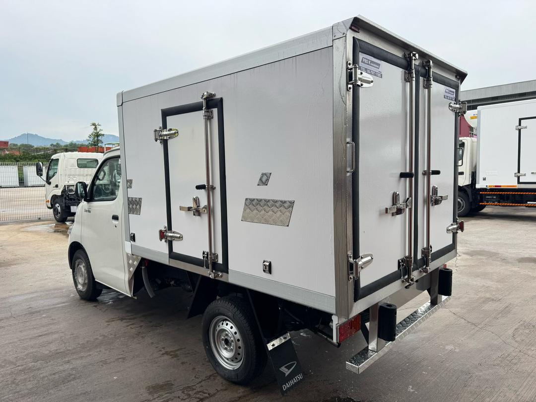 A white Daihatsu Gran Max box truck with silver metal doors, black trim, and heavy-duty latches, photographed outdoors on a paved lot with other trucks in the background.