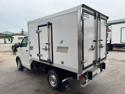 A white Daihatsu Gran Max box truck with silver metal doors, black trim, and heavy-duty latches, photographed outdoors on a paved lot with other trucks in the background.