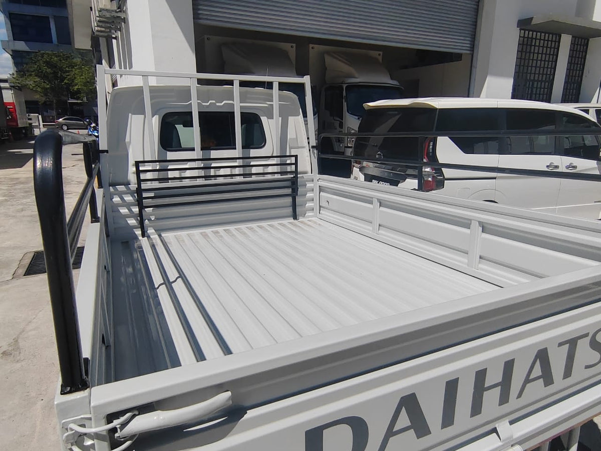 White Daihatsu utility truck bed with a slatted floor and white metal side rails, photographed outdoors in front of a building with other vehicles visible.