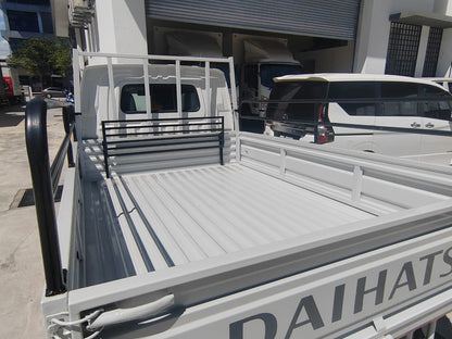 White Daihatsu utility truck bed with a slatted floor and white metal side rails, photographed outdoors in front of a building with other vehicles visible.