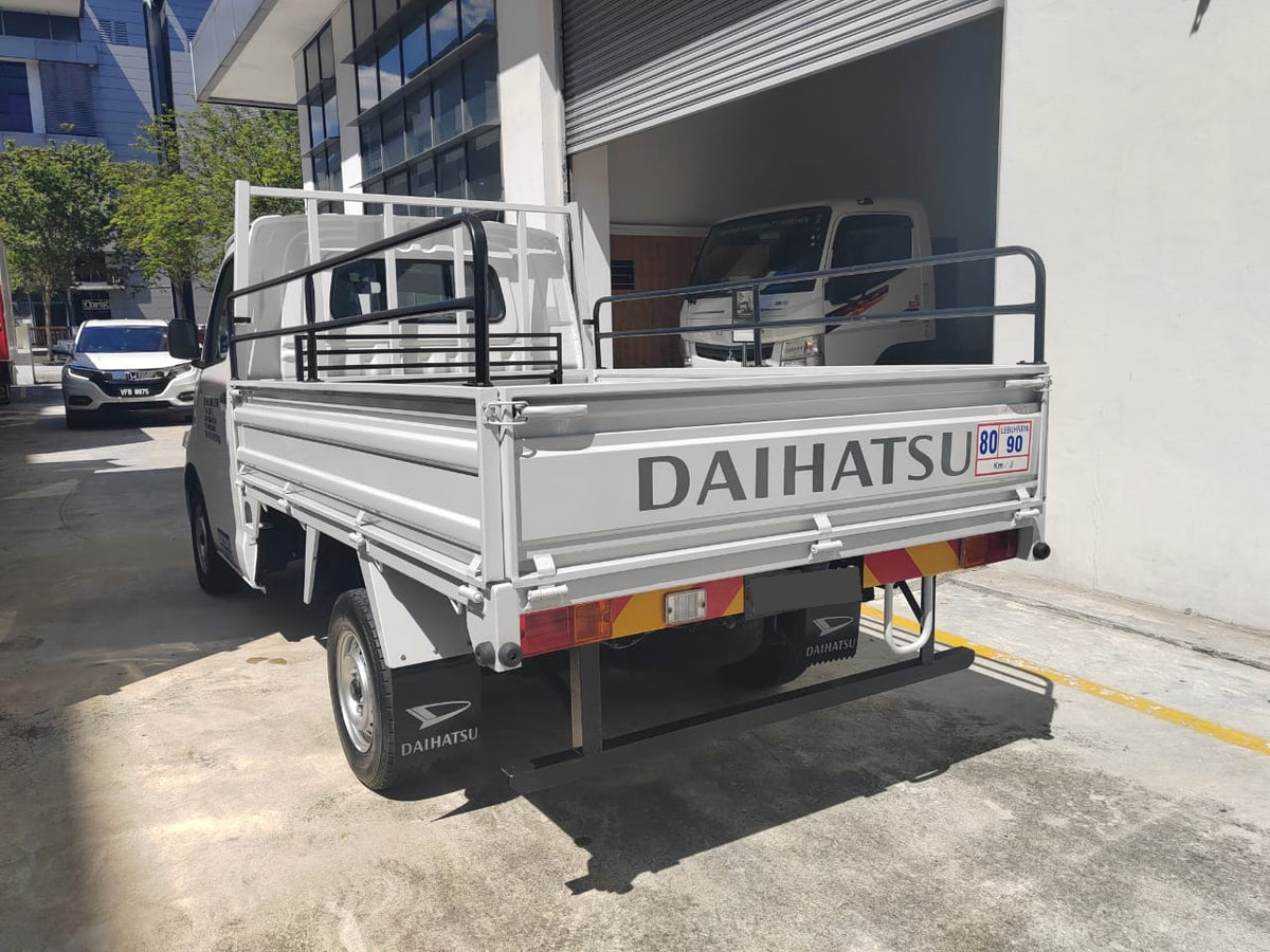 A white Daihatsu Gran Max utility truck with a flatbed cargo bed and rear ramp, photographed outdoors in front of a building with a garage door open.