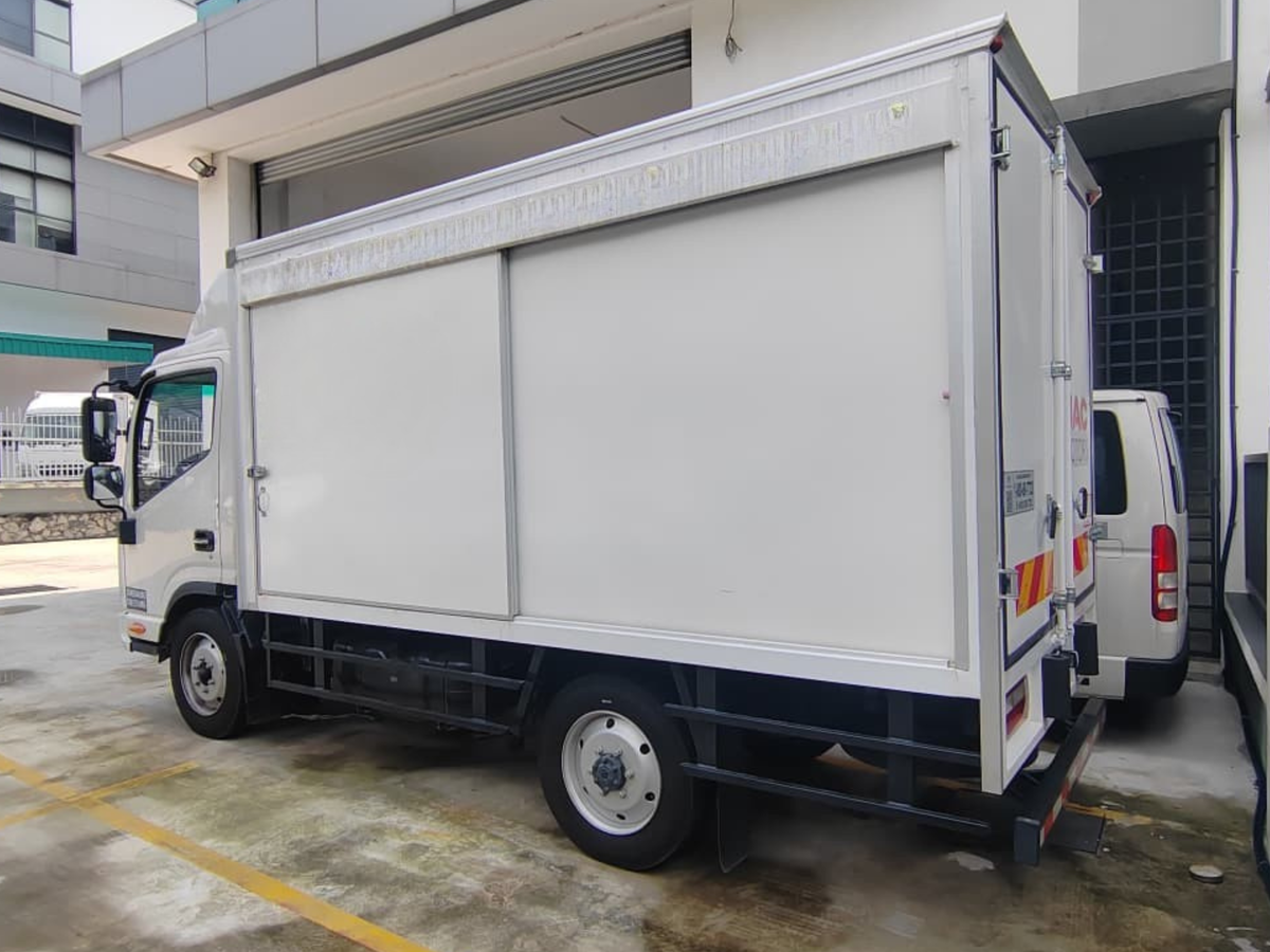 A white JAC N50 box bonded truck parked outdoors in a lot next to a building, with a second white vehicle partially visible behind it.