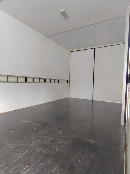 An empty white van or trailer interior with a dark gray floor, white walls, a sliding door, and a ceiling light.